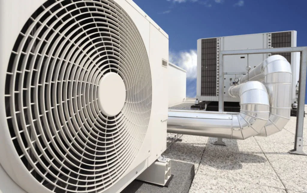 Ventilador de una unidad exterior de climatización junto a conductos metálicos en la cubierta de un edificio