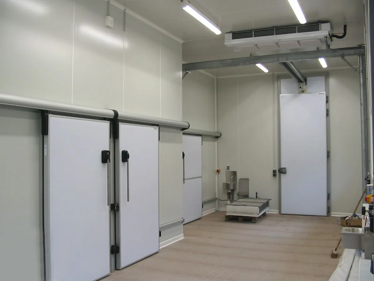 Sala de cámaras frigoríficas con puertas correderas aisladas, evaporador en el techo y un palé en el suelo