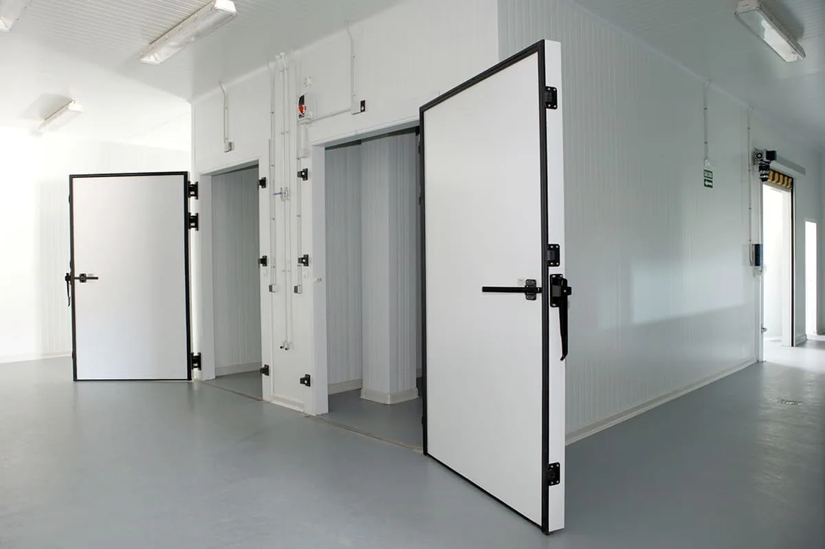 Dos puertas batientes abiertas de cámaras frigoríficas en una sala con paredes de panel blanco