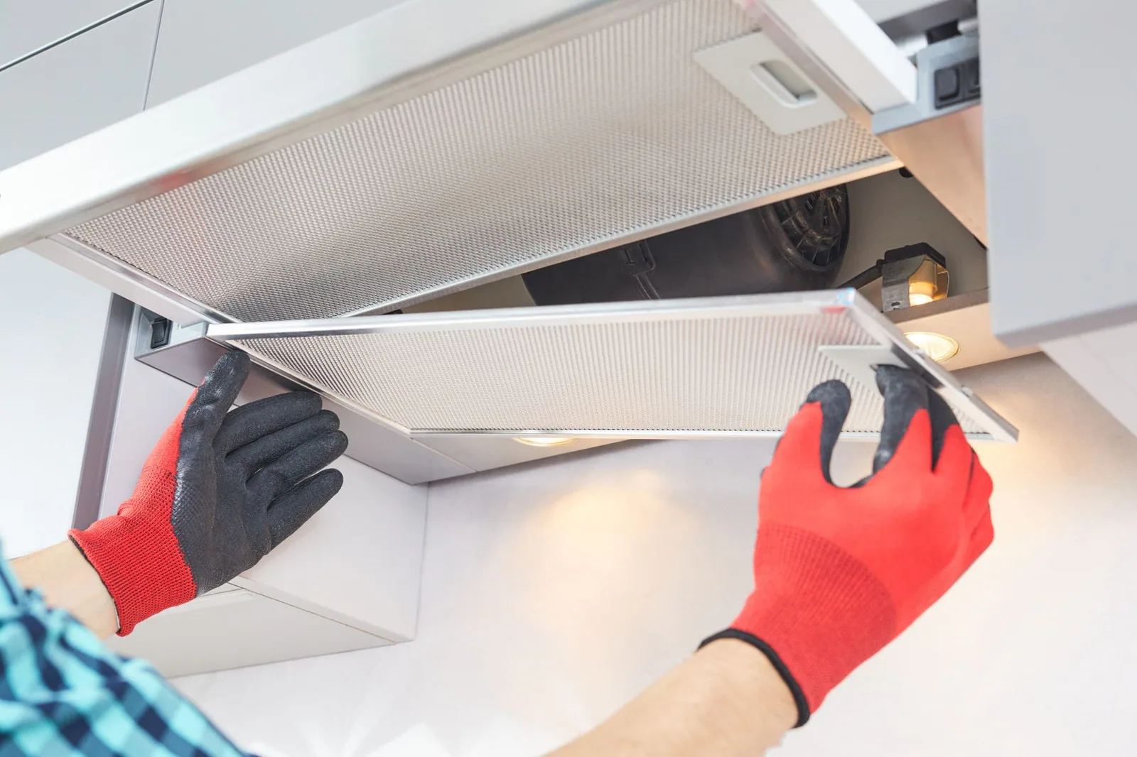 Manos con guantes rojos retirando el filtro metálico de una campana extractora y dejando ver el motor