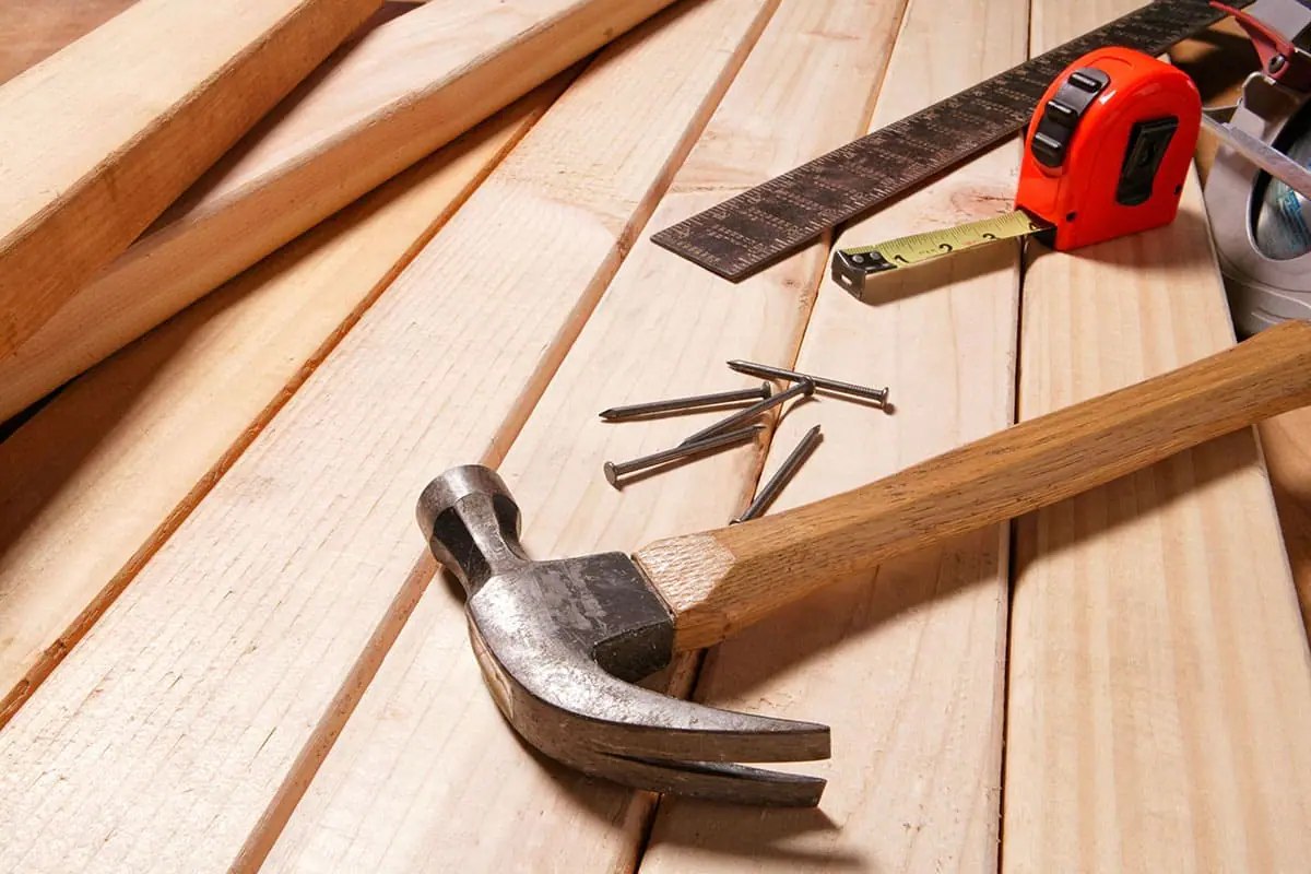 Martillo, clavos, flexómetro rojo y regla metálica sobre listones de madera de pino