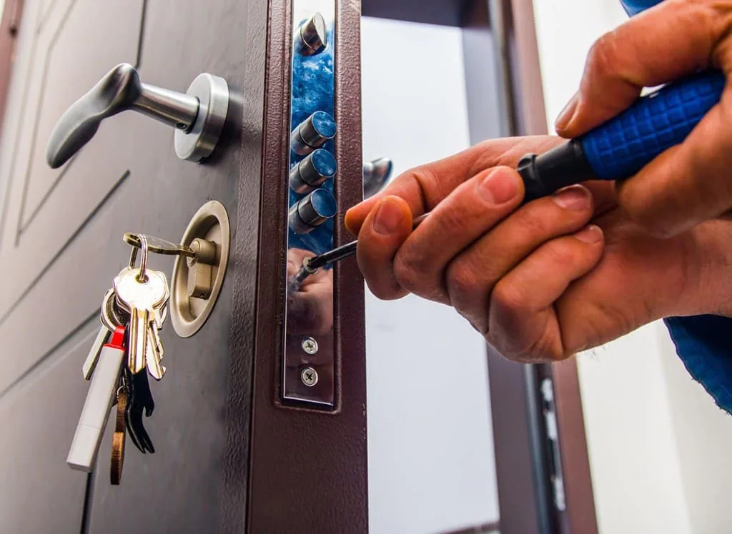 Mano ajustando con destornillador una cerradura de pestillos múltiples en una puerta de seguridad con las llaves puestas