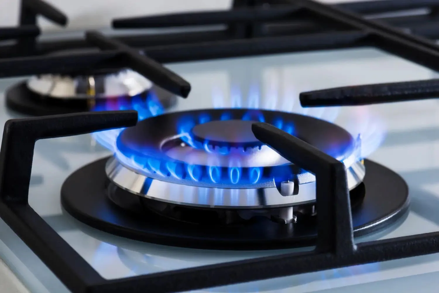 Quemador de gas encendido con llama azul bajo las parrillas de hierro fundido de una placa blanca