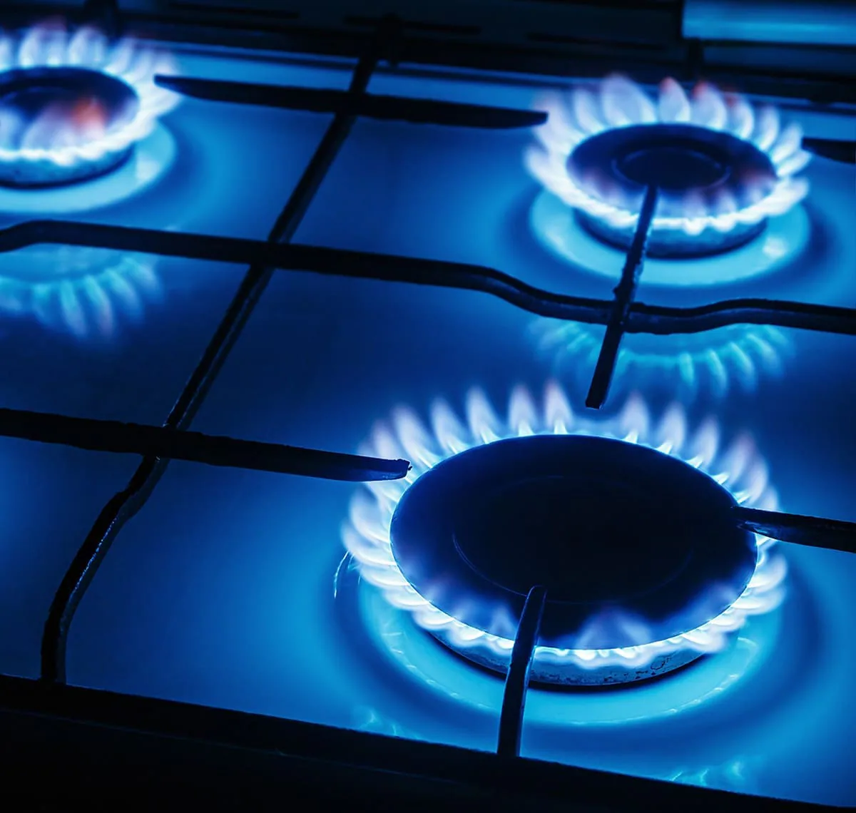 Tres quemadores de una cocina de gas encendidos con llama azul bajo la parrilla en penumbra