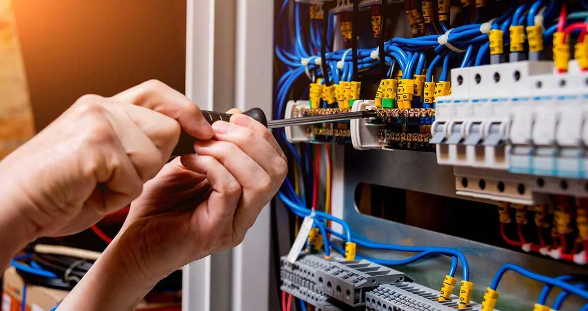 Manos apretando con destornillador los bornes de un cuadro eléctrico con cableado azul, imagen ilustrativa del servicio de electricistas en Tenerife