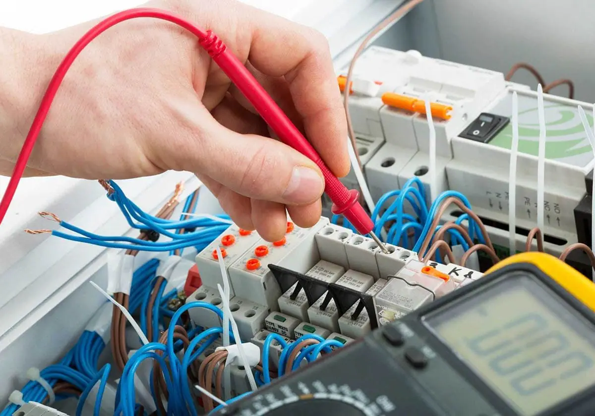 Punta roja de un polímetro comprobando los bornes de un cuadro eléctrico con cables azules