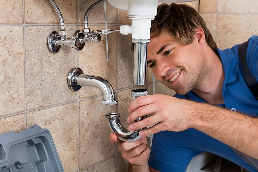 Operario montando el sifón cromado de un lavabo bajo dos llaves de escuadra con latiguillos