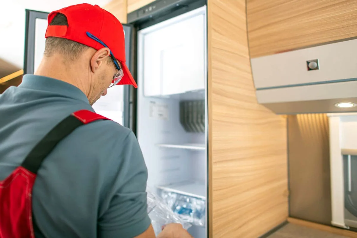 Técnico de espaldas con gorra roja revisando el interior de un frigorífico empotrado en un mueble de madera