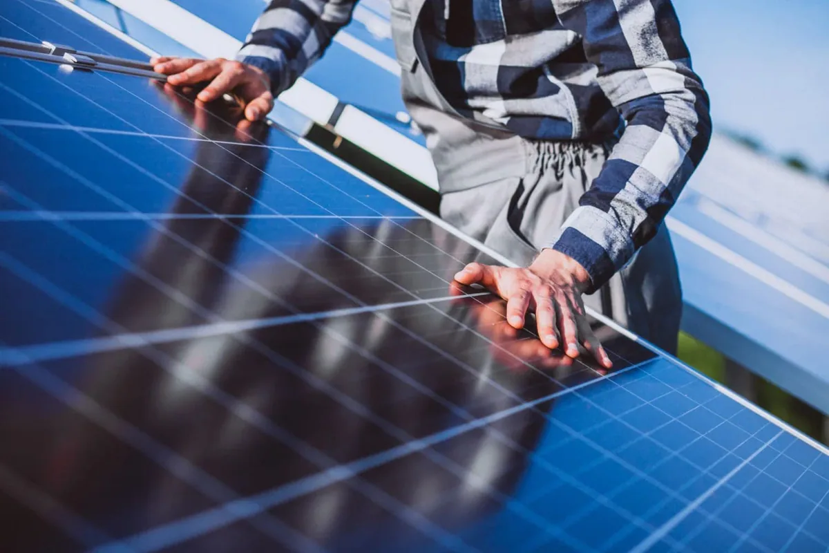 Persona sujetando un módulo fotovoltaico junto a una fila de paneles