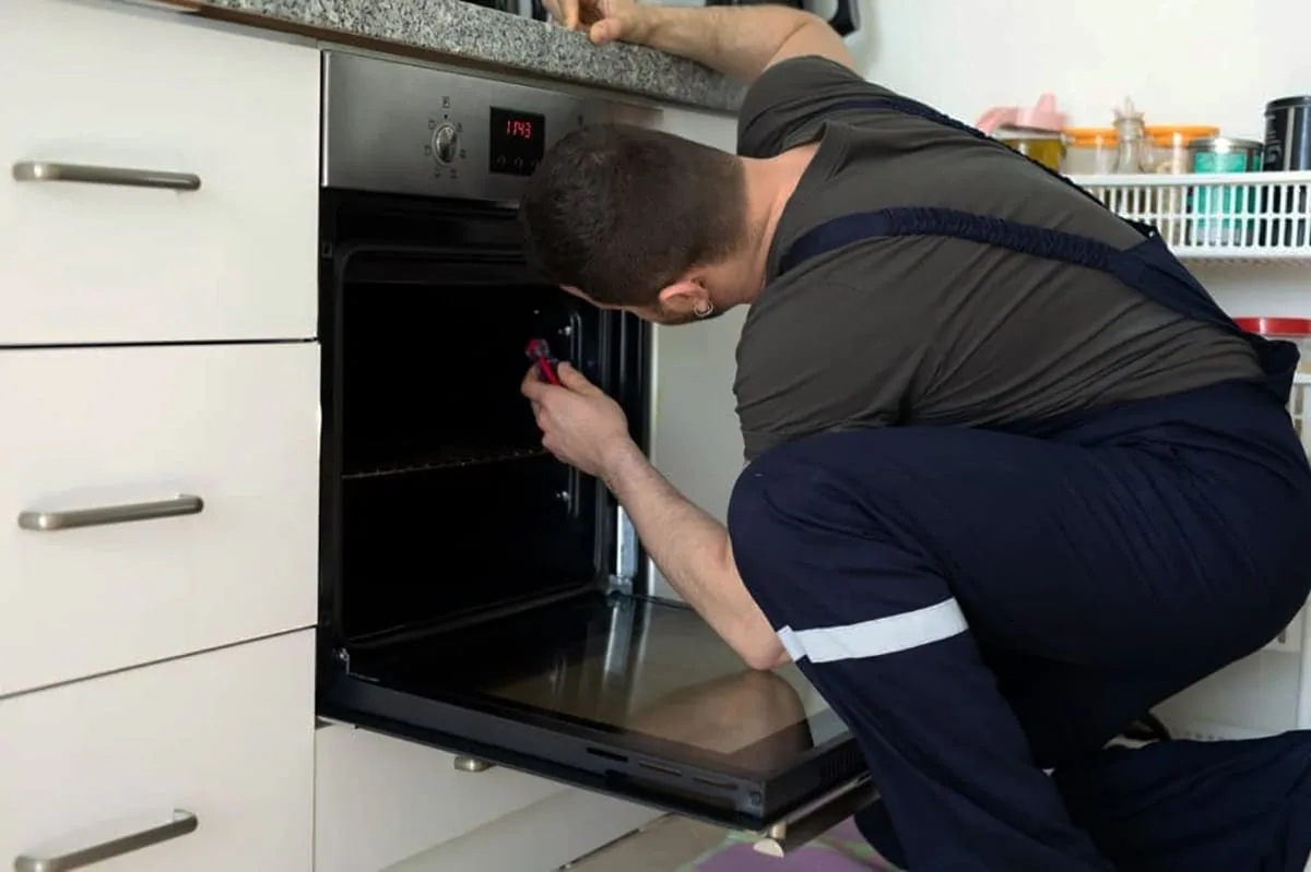 Técnico de espaldas con peto oscuro que revisa con una herramienta roja el interior de un horno empotrado abierto