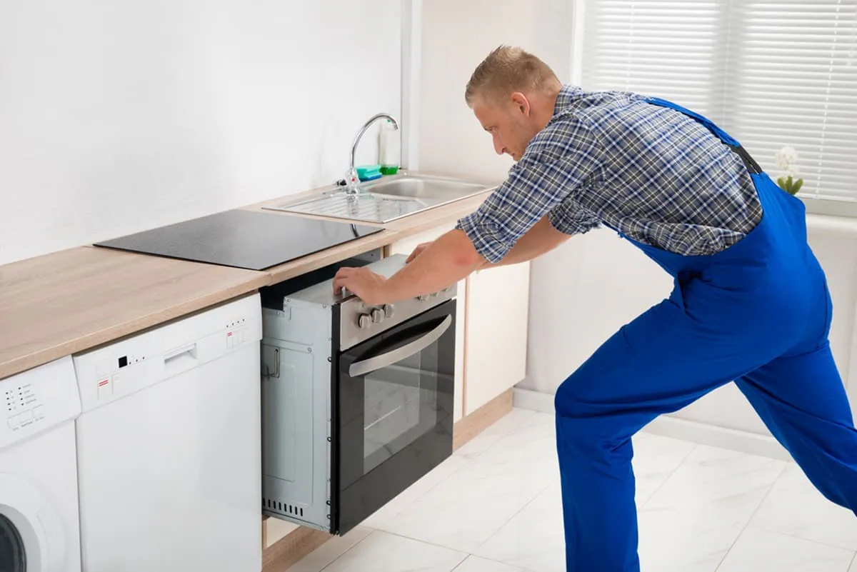 Técnico con peto azul encajando un horno de acero inoxidable en el hueco de un mueble de cocina