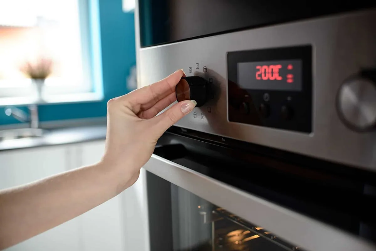 Mano que gira el mando de un horno de acero inoxidable con la pantalla marcando doscientos grados