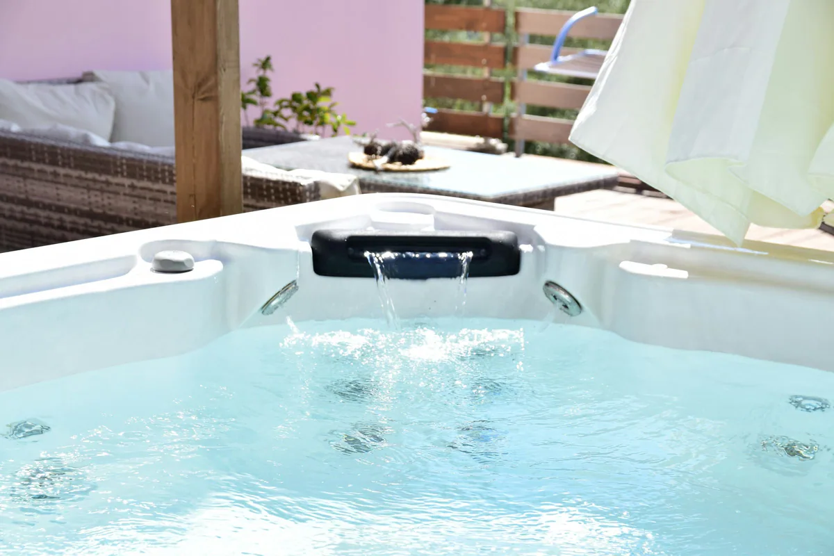 Jacuzzi exterior blanco con cascada y chorros de hidromasaje en funcionamiento junto a una terraza