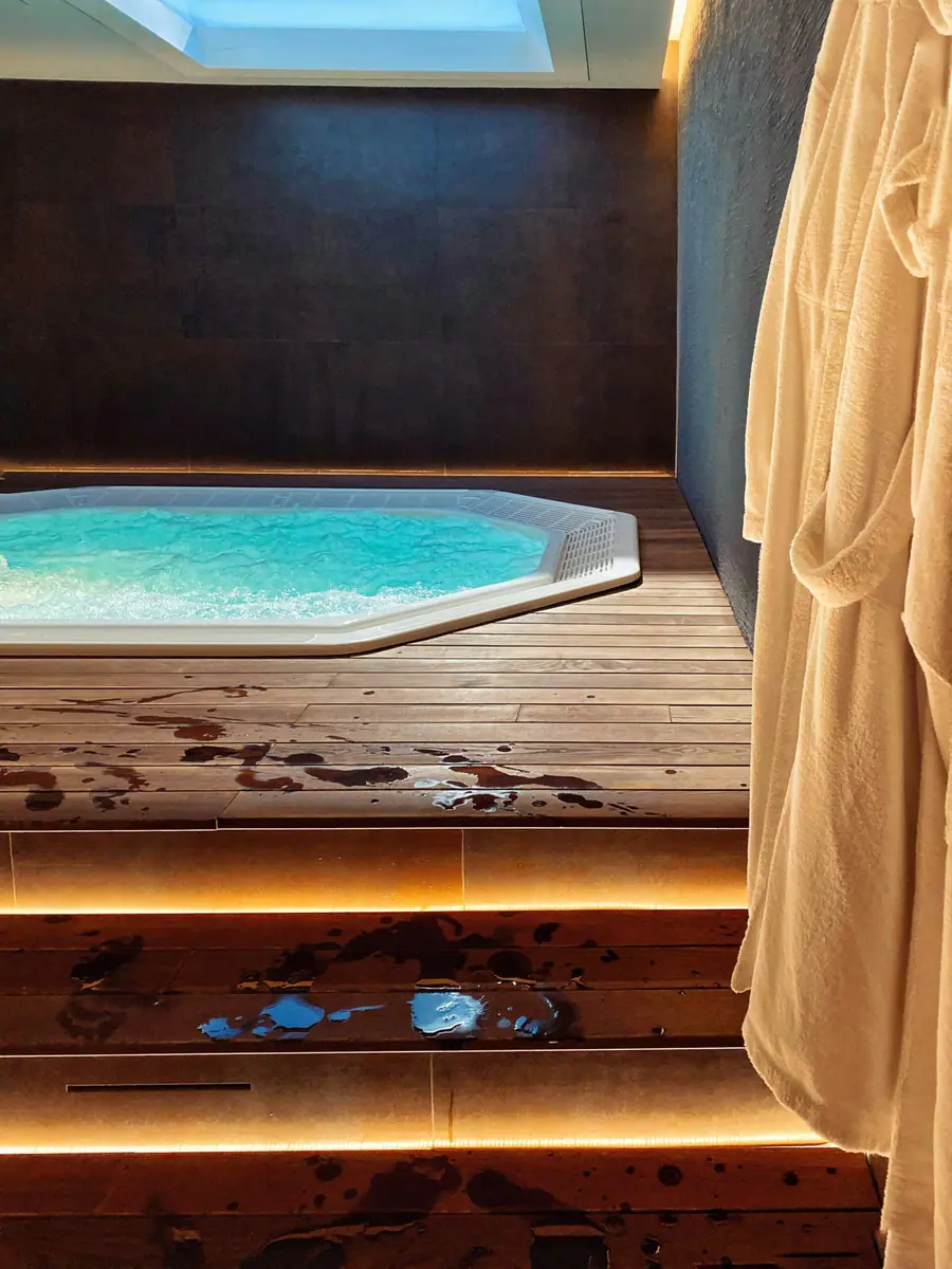 Jacuzzi octogonal encastrado en una tarima de madera bajo un lucernario, con albornoces colgados