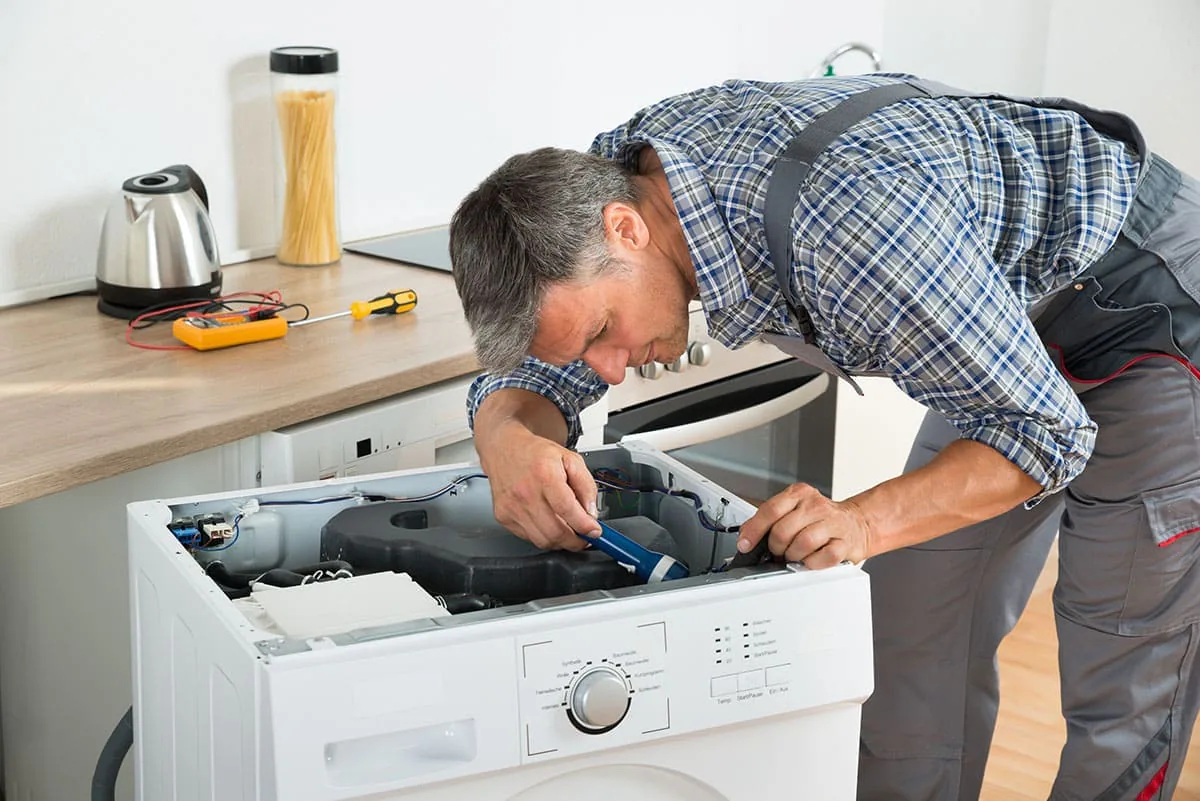 Técnico con camisa de cuadros reparando con un destornillador el interior de una lavadora sin tapa superior