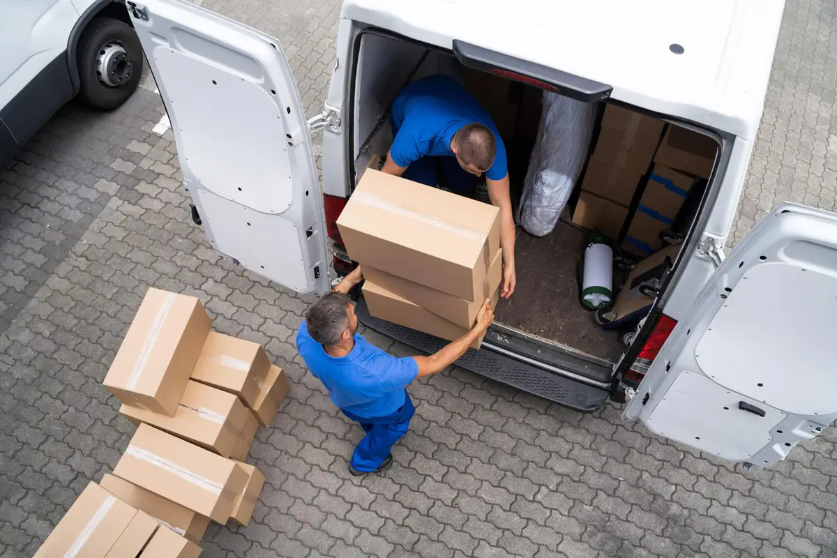 Vista cenital de dos operarios que se pasan cajas de cartón para cargarlas en una furgoneta blanca
