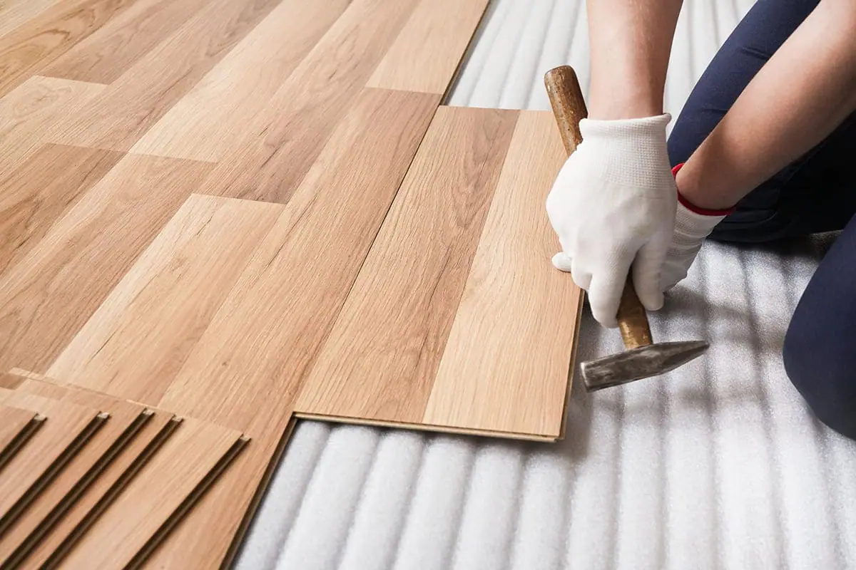 Manos con guantes blancos encajando con martillo las lamas de un suelo laminado sobre una base de espuma