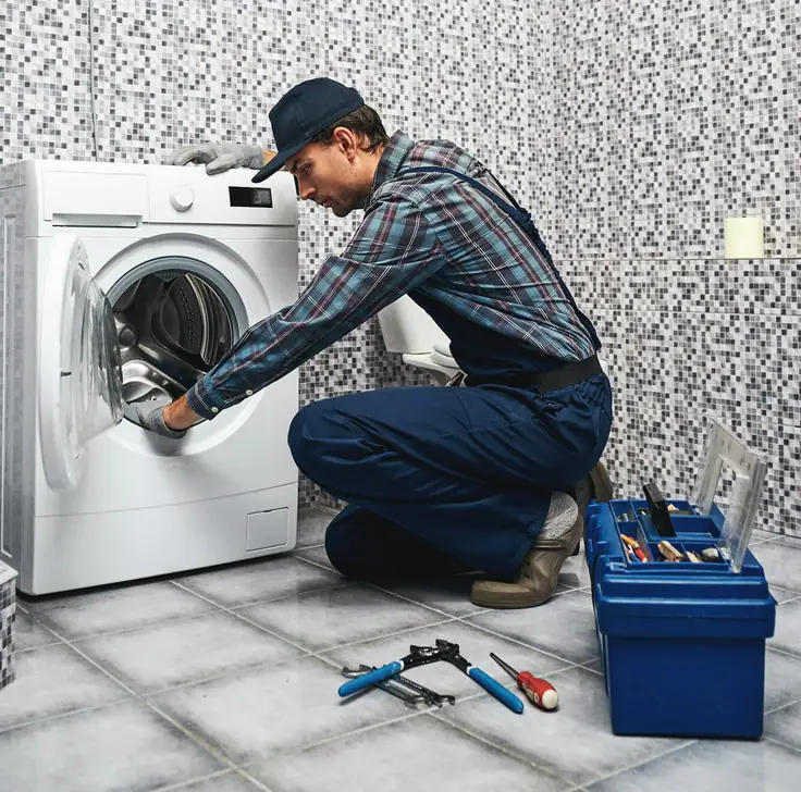Técnico con gorra y guantes que revisa el tambor de una máquina de carga frontal en un baño