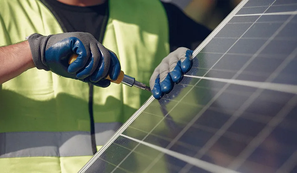 Manos con guantes ajustando con un destornillador el marco de un panel solar